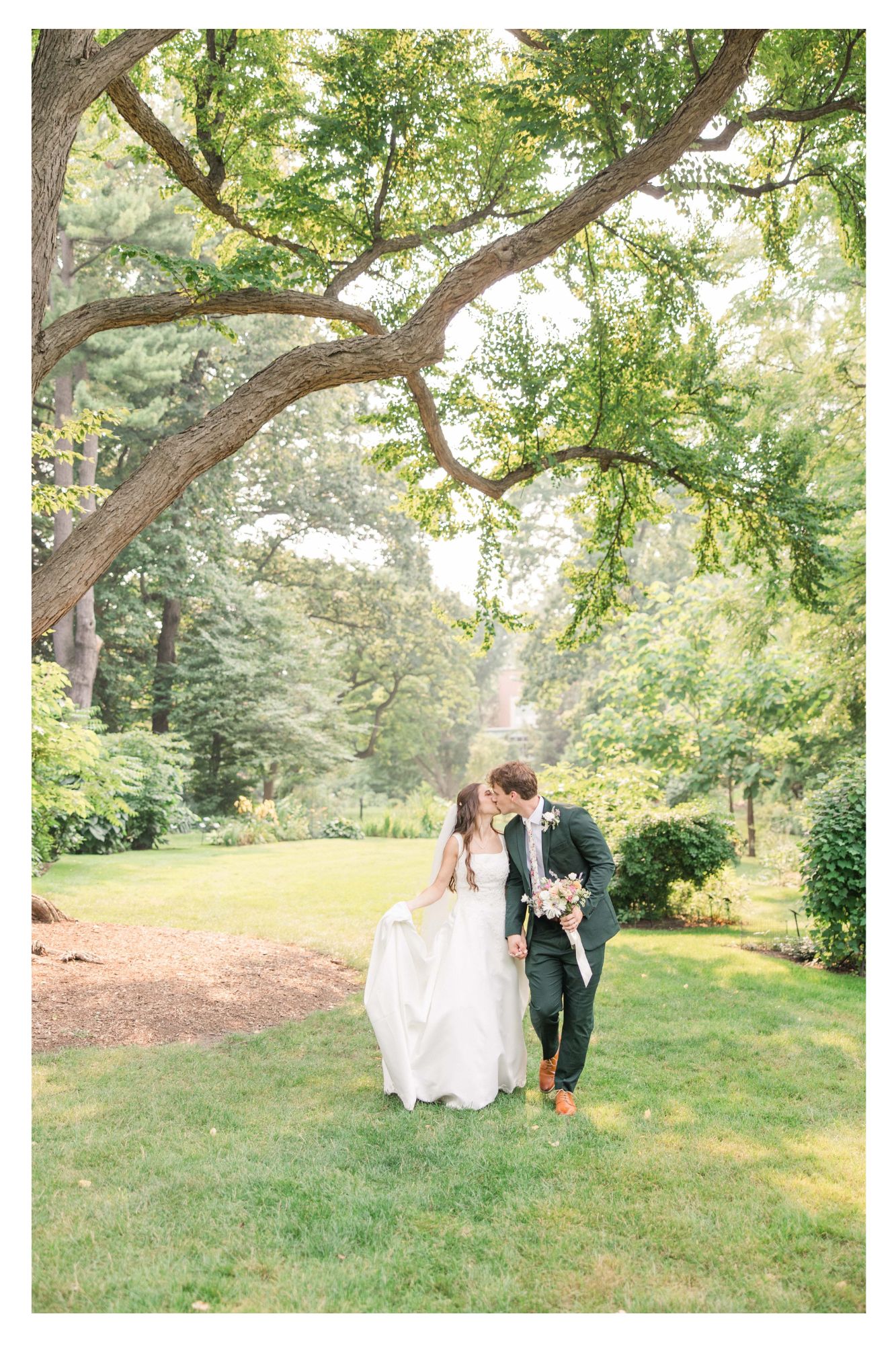 Bride and groom walking and kissing under a beautiful tree in the MSU gardens